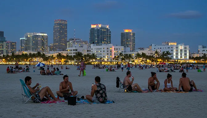 A diverse group on a Miami Beach cannabis-friendly section at dusk, using Delta-8 vapes and CBD drinks, with the skyline and art-deco buildings in the background | Hurcann