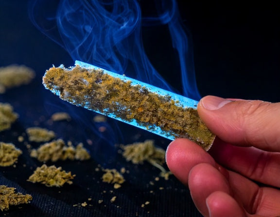 Four infused pre-rolls (kief, wax, oil, distillate) on a wooden tray with cannabis leaves and a lighter.