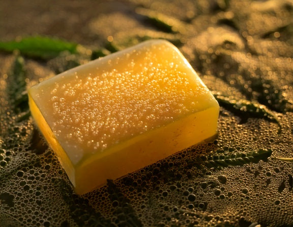 CBD soap bar on hemp leaves with silky bubbles and a golden glow, symbolizing wellness and serenity.