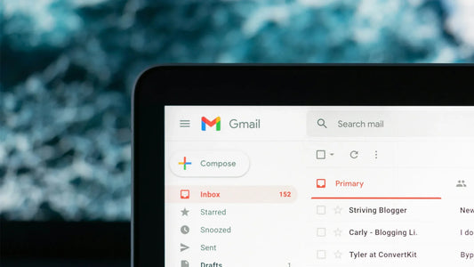 A close-up of a laptop screen displaying a Gmail inbox with 152 unread emails, showing the compose button, inbox, and email list, with a blurred blue background | Hurcann