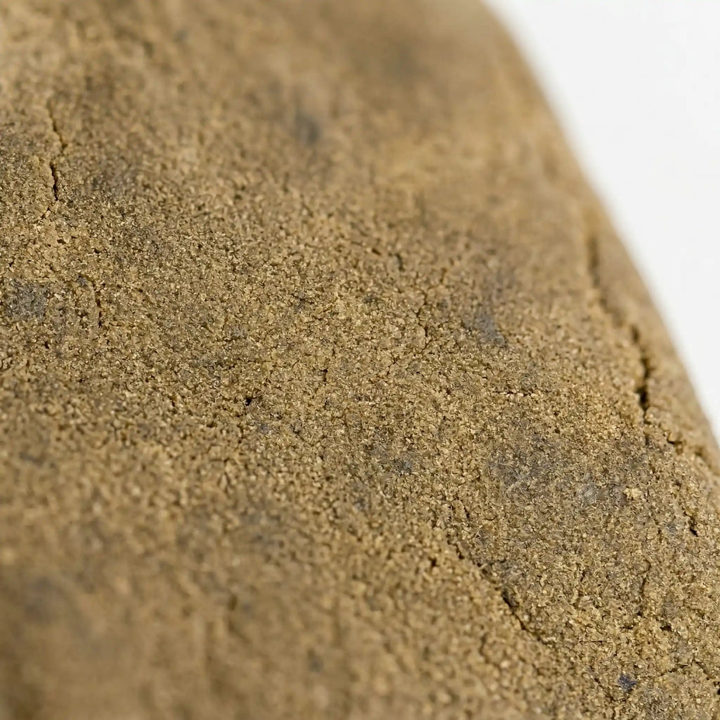 THCA bubble hash close-up texture — fine granular sandy surface with natural stress fractures and trichome crystal detail