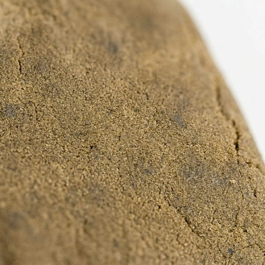 THCA bubble hash close-up texture — fine granular sandy surface with natural stress fractures and trichome crystal detail