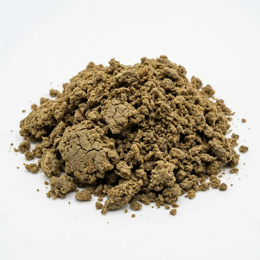 Large loose mound of crumbled CBD bubble hash on a white background, warm olive-brown granular texture with varied chunk sizes scattered around the base | Hurcann