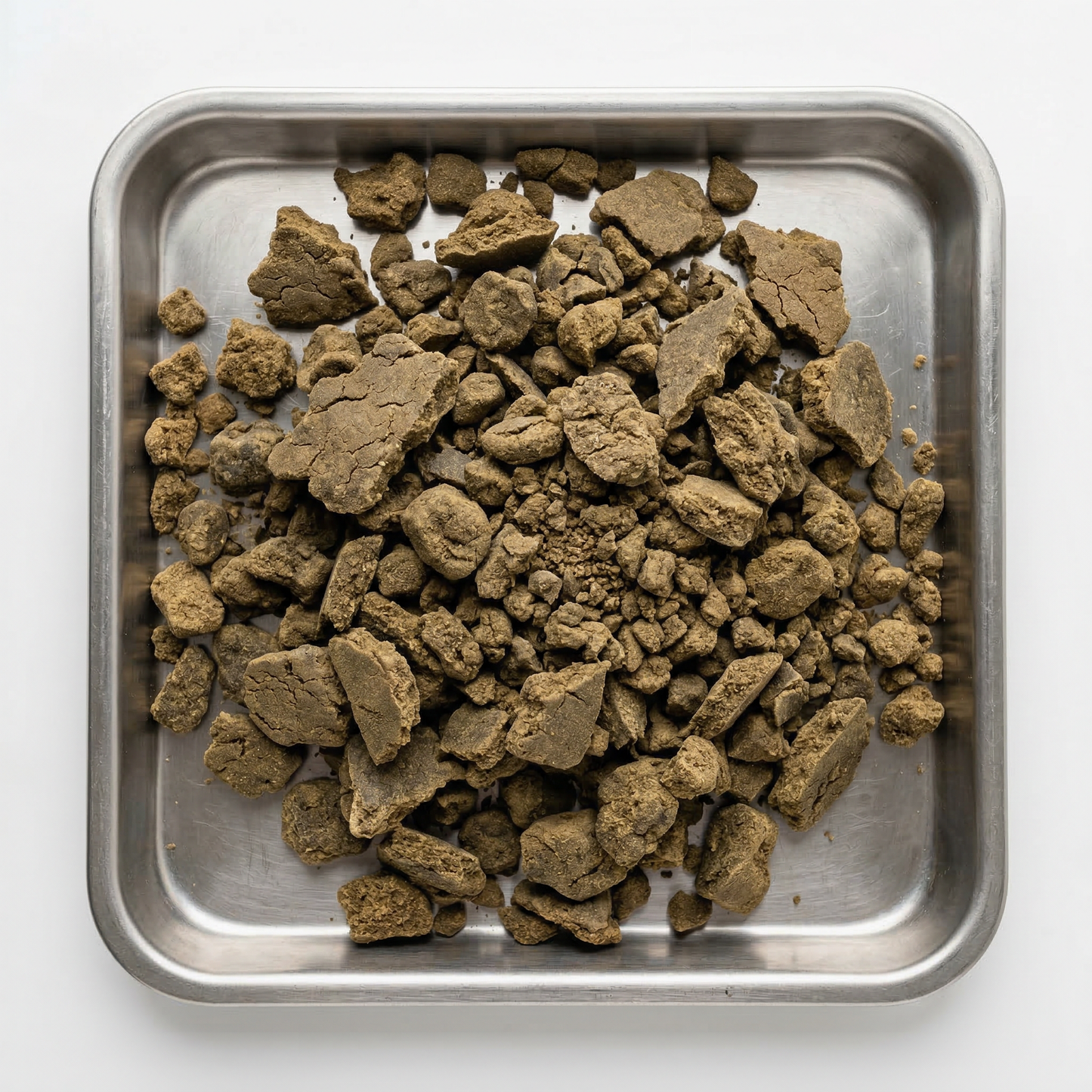 Overhead view of bulk CBD bubble hash chunks and crumbled pieces filling a square stainless steel tray, olive-brown tones with matte cracked texture, clean white background
