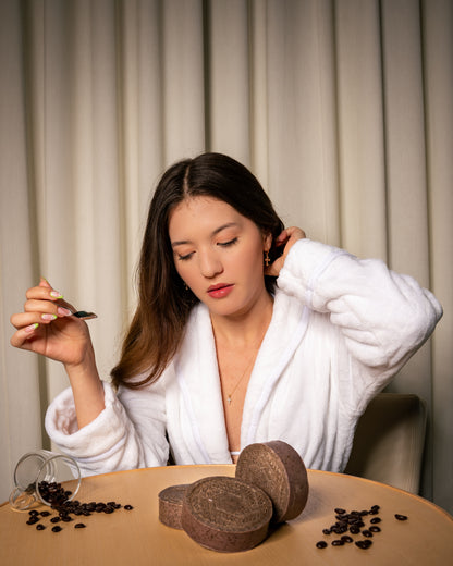 Smiling woman holding a coffee-infused CBD soap bar near her face, showcasing its natural ingredients, exfoliating benefits, and energizing coffee scent.