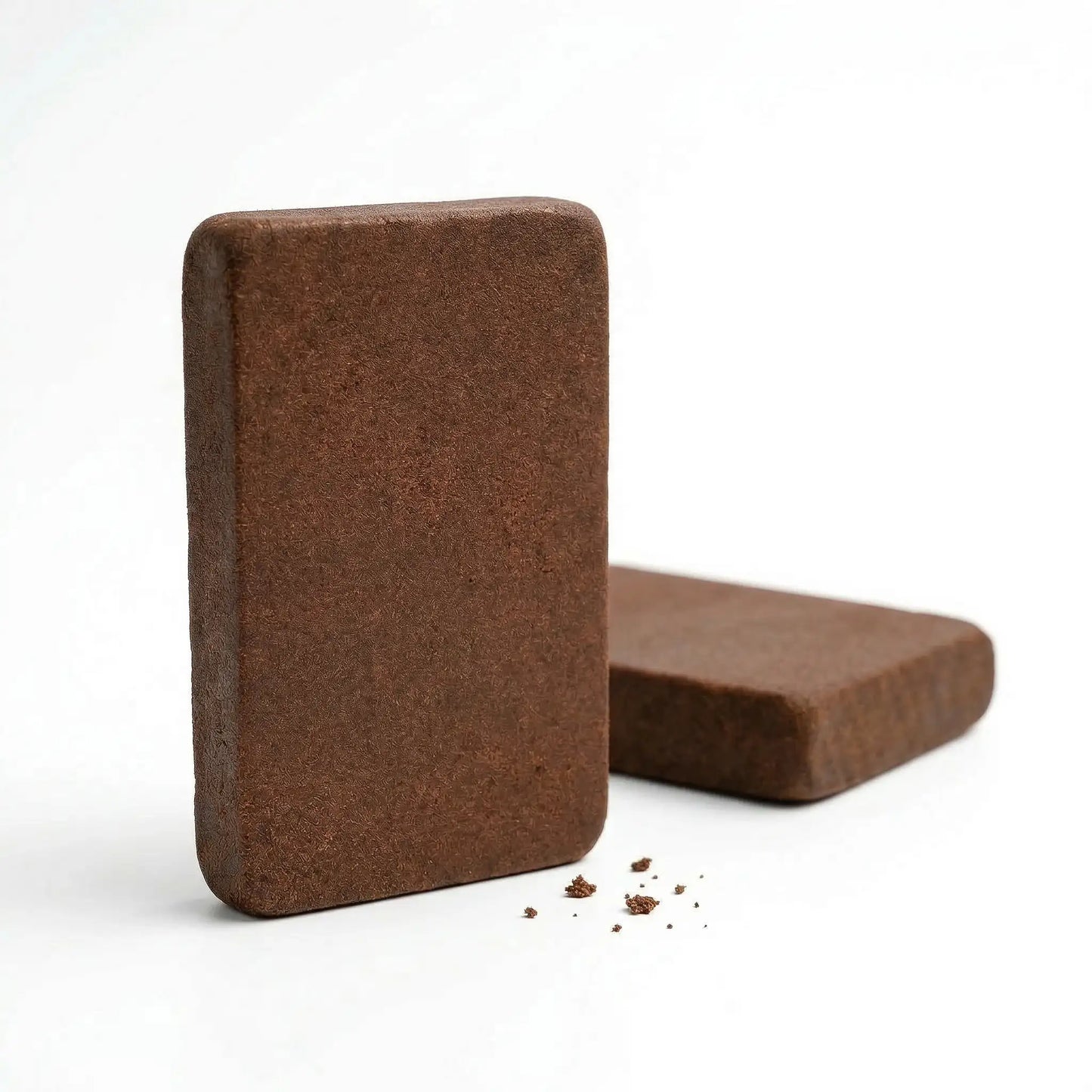 Two CBD Lebanese red hash slabs on a white surface, one standing upright showing full height and smooth chocolate-brown matte fibrous surface, second slab lying flat behind it | Hurcann