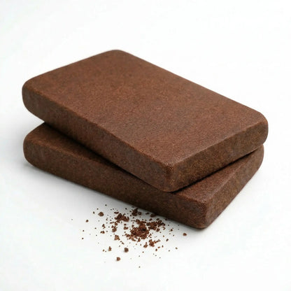 Two bulk wholesale THCA Lebanese red hash slabs stacked on a white background, smooth chocolate-brown matte fibrous surface, clean rounded corners, fine granular crumble scattered at the base — bulk THCA hash wholesale supply